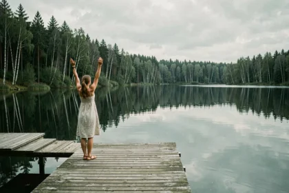 Femme se détendant sur un ponton en bois au bord du lac de Vassivière entourée de forêts de pins